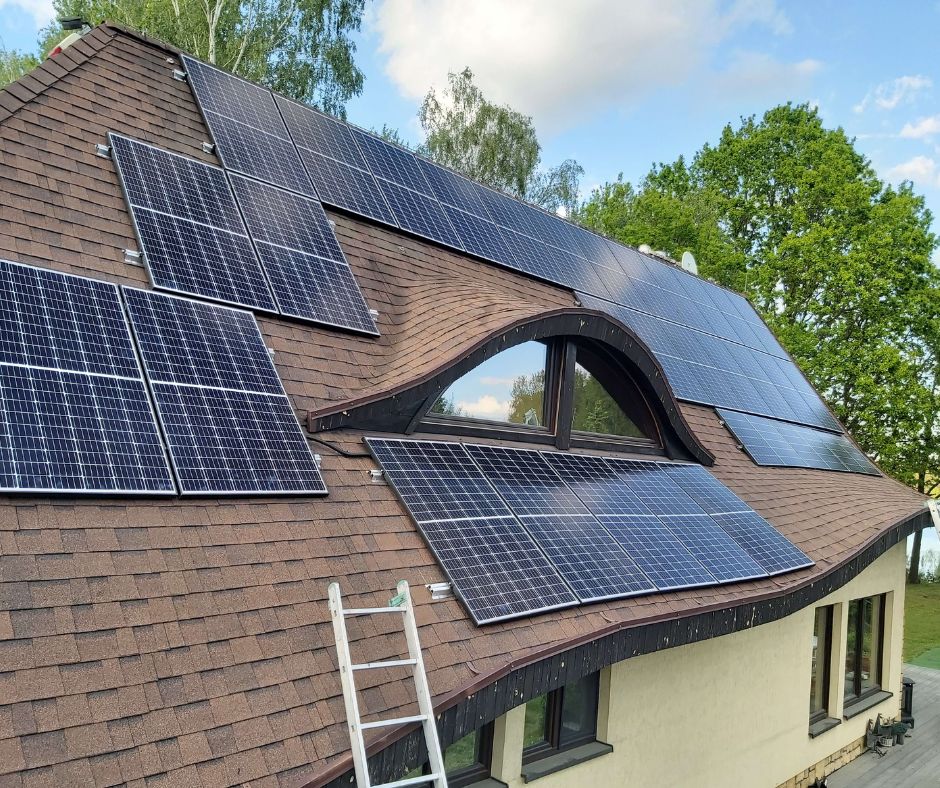 Panele fotowoltaiczne JA Solar na dachu domu jednorodzinnego. Obok drabina oparta o dach